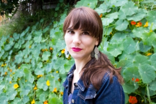 Writer Lauren Eggert-Crowe Seated in front of foliage with orange flowers Looking at Camera