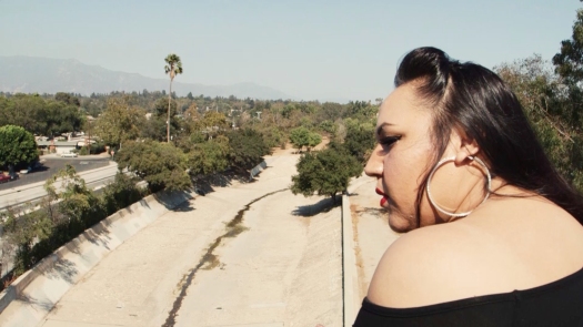 A Latina with hoop earrings is in profile, overlooking a dry wash