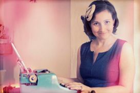 Filtered photo of writer Rachael Rifkin sitting at a blue tablet typewriter, smiling